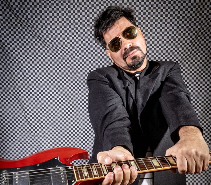 Beto Aguilar empuñando una guitarra roja sobre un fondo gris